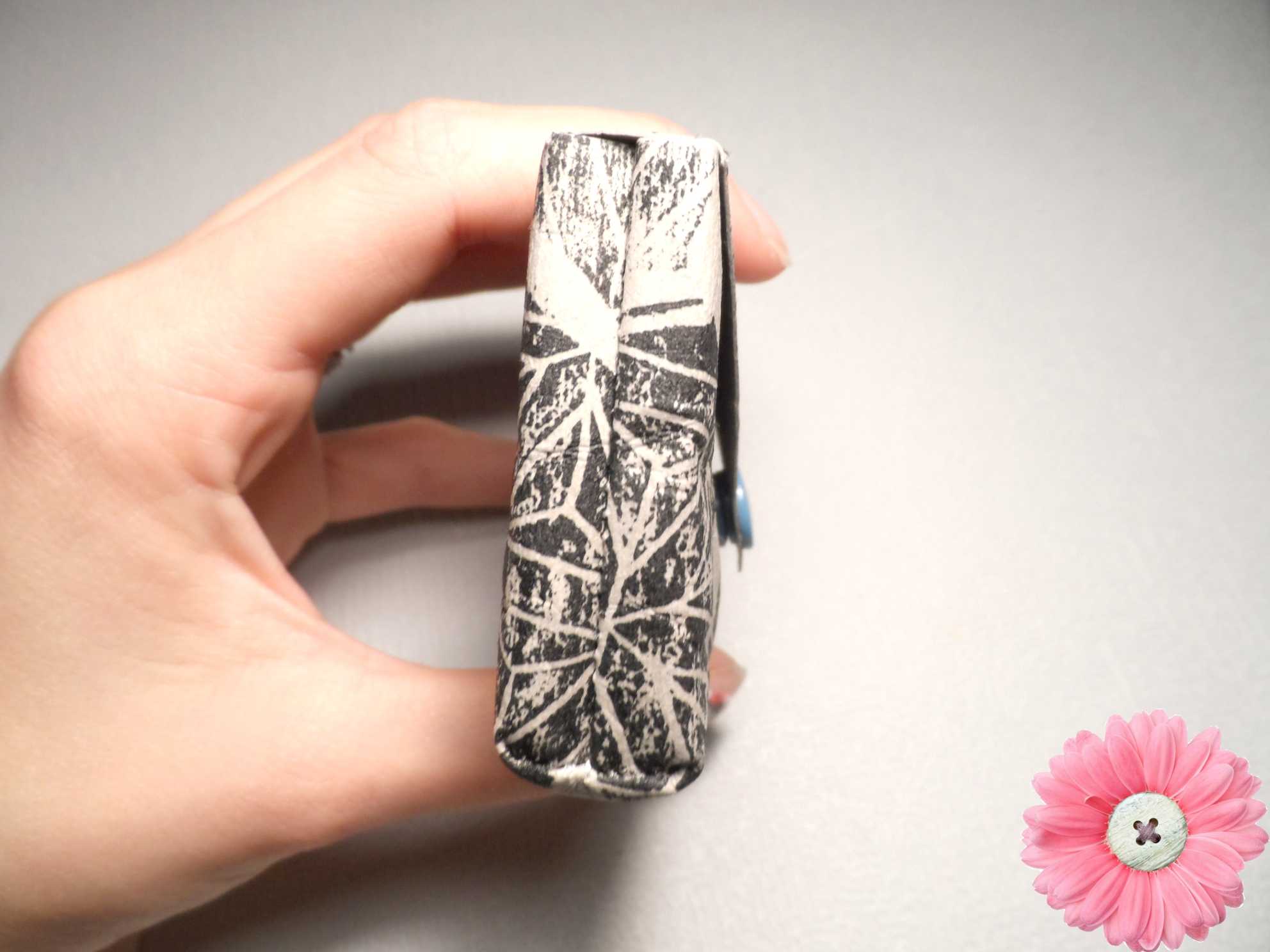 Eine Hand hält ein kleines schwarz-weiß gemustertes Stofftäschchen mit blauem Knopf vor hellem Hintergrund