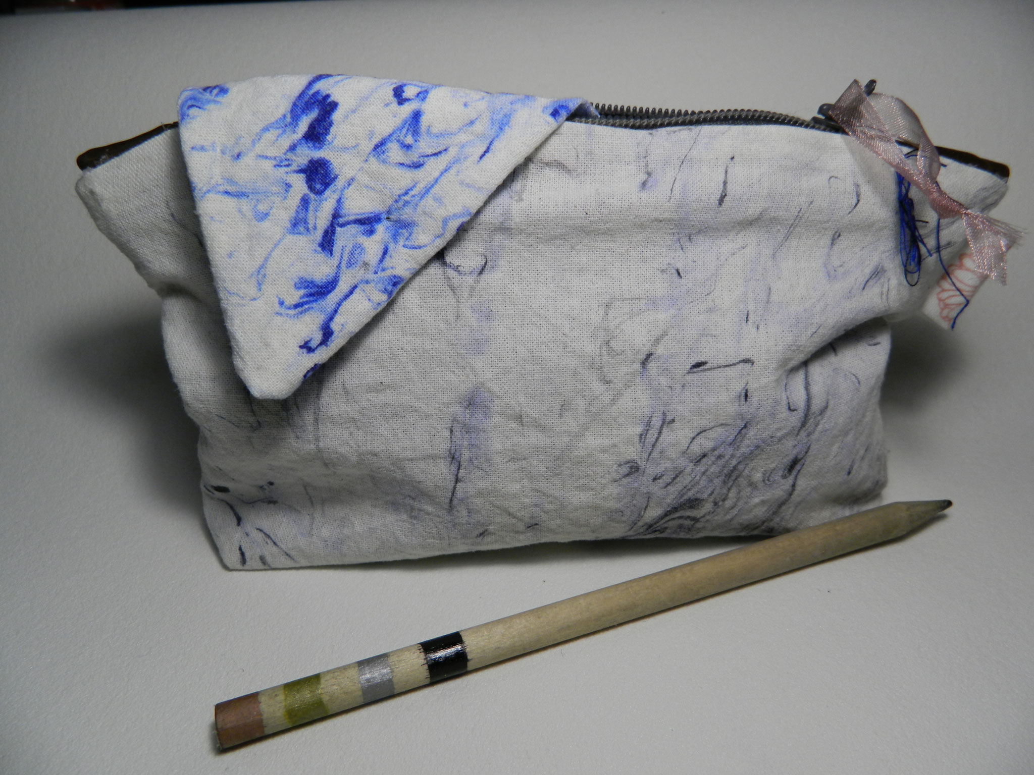 Marmoriertes blau-weißes Stofftäschchen mit Reißverschluss neben einem gestreiften Stift, ruhige Bastelstimmung